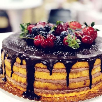 Pastel con cobertura de chocolate y tres capas de relleno de fresa entre la masa y topping de frutas